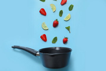 Saucepan and ingredients for preparing strawberry compote on blue background