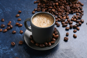 Cup of hot espresso and coffee beans on blue background
