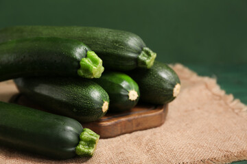 Wooden board with many fresh zucchini on green background