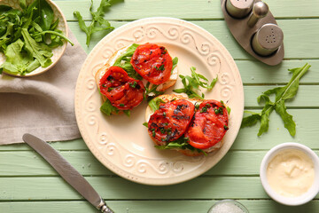 Plate of sandwiches with tasty grilled tomatoes and arugula on green wooden background