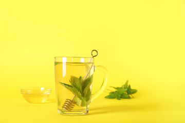 Cup of fresh mint tea with honey on yellow background