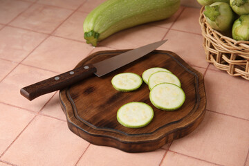 Wooden board with slices of raw zucchini on beige tile background