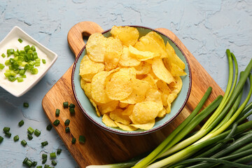 Bowl of tasty sour cream with sliced green onion and potato chips on blue background