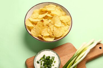 Bowl of tasty sour cream with sliced scallion and potato chips on green background