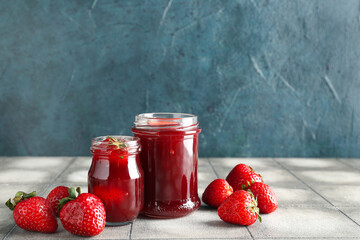 Jars of sweet strawberry jam and fresh berries on table