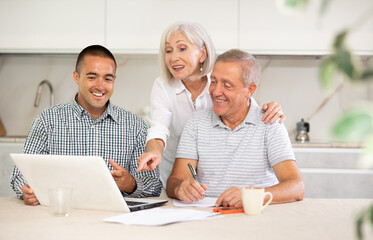 Young salesman explaining terms of deal to elderly couple sitting in kitchen. Health insurance concept