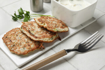 Board of tasty zucchini fritters with sour cream on white tile background