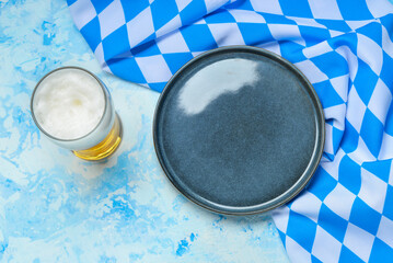 Mug of beer, empty plate and checkered tablecloth on light blue table