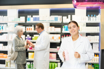 Obraz premium In pharmacy, young female specialist holds in hands and presents shows new effective remedy for moisturizing delicate skin of children