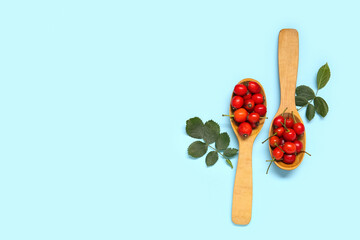 Wooden spoons with fresh rose hip berries and leaves on blue background