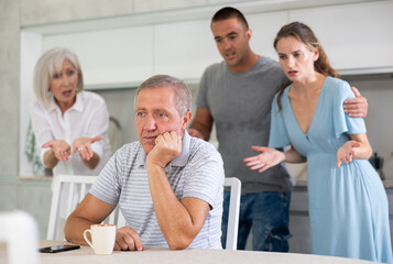 Adult man sits at table in kitchen and pretends that he does not hear anything from his relatives