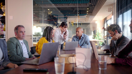 Diverse team of professionals engages in a productive meeting, utilizing laptops for data analysis and collaborative discussion in a vibrant, modern office environment