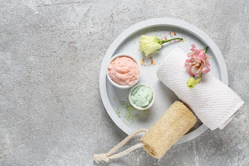 Tray with body scrubs, bath supplies and flowers on grunge background