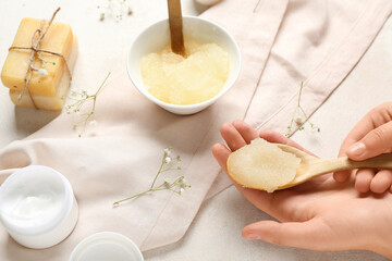 Female hands with body scrub and cosmetic products on light background