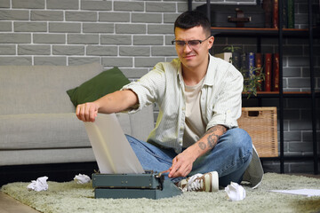 Displeased male author with vintage typewriter sitting on floor at home