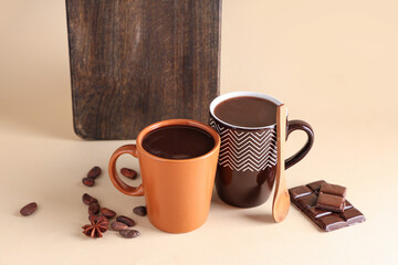 Wooden board with cups of tasty hot chocolate, spoon and cocoa beans on beige background