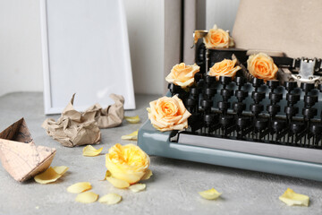 Vintage typewriter with craft paper, photo frame and roses on grey grunge table near white wall