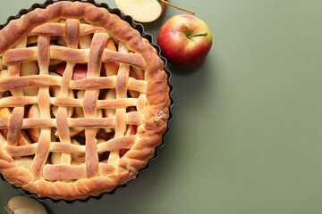 Baking dish with tasty homemade apple pie and fruits on green background
