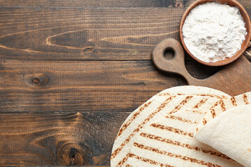 Composition with fresh lavash and bowl of flour on wooden background