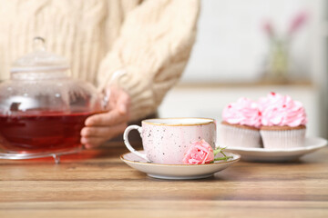 Young woman holding teapot with hibiscus tea in kitchen