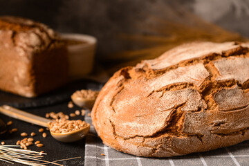 Fresh bread with spoon of wheat grains on black table