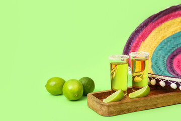 Mexican sombrero, limes and wooden tray with shots of tequila on green background