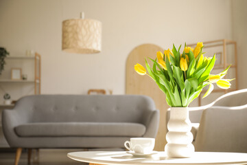 Vase with tulips and cup of coffee on table in living room