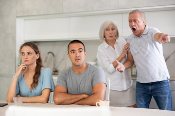 Obraz premium Girl and guy are sitting in kitchen and do not listen to their father and mother