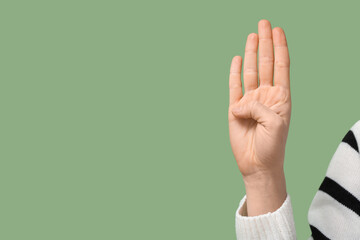 Deaf mute woman using sign language on green background, closeup