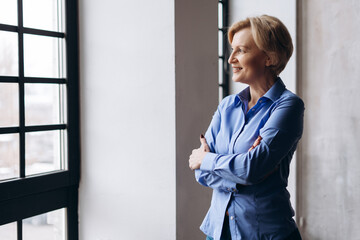 Portrait of happy blonde mature lady standing with arms folded