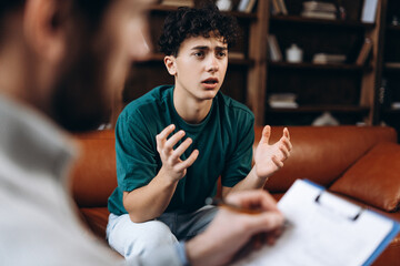 Teenage boy talking with professional male psychoanalyst during therapy session in the office