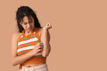 Young African-American woman with skin allergy scratching herself on brown background
