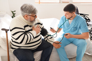 Obraz premium Young caregiver measuring blood pressure of senior man in bedroom
