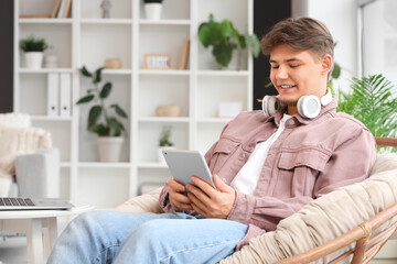 Male student with tablet computer studying online in armchair at home