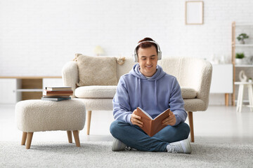 Young man listening music and reading book on floor in living room