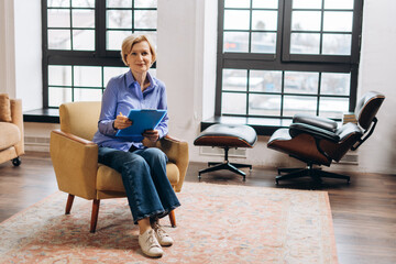 Smiling female psychologist posing to camera sitting in armchair in her office