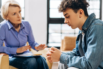 Middle aged female psychologist working with teenager boy in office while talking