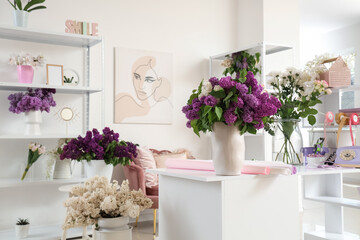 Vases with bouquet of lilacs and wrapping paper on table in florist studio