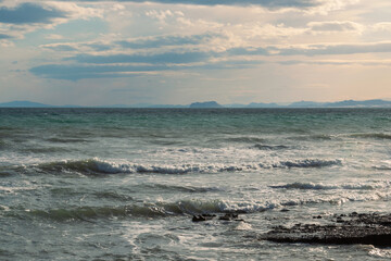 Waves of the sea breaking on the shore with lines of mountains in the background. Summer seascape inviting to rest and relaxation