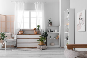 Interior of stylish living room with armchair, shelving unit and chest of drawers