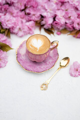 Pink cherry blossoms and cup of coffee with heart-shaped latte art on white background. Spring flat lay with copy space