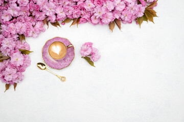 Pink cherry blossoms and cup of coffee with heart-shaped latte art on white background. Spring flat lay with copy space