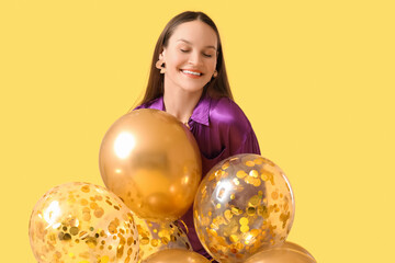 Fototapeta premium Happy young woman with air balloons on yellow background