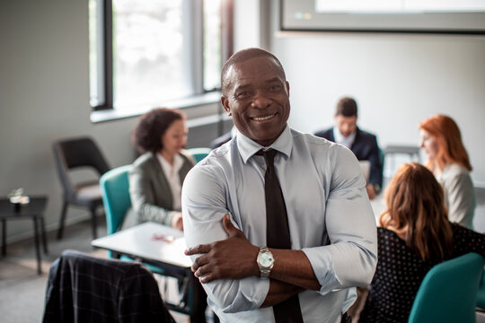 Portrait of a confident businessman standing in office with team working in background