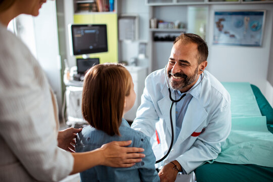 Smiling doctor using stethoscope to check young girl at medical clinic with mother nearby