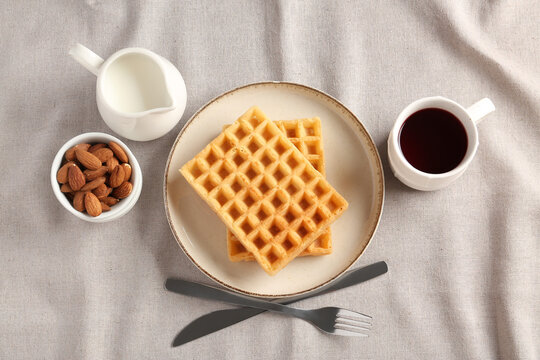 Plate with tasty Belgian waffles, almond and cup of coffee on table
