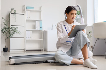 Female doctor writing in clipboard near treadmill at hospital