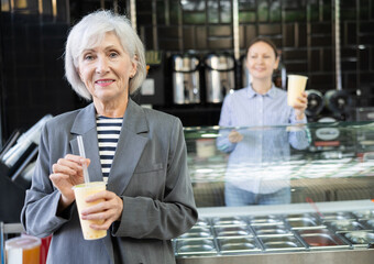 Near bar, senior woman drinks tonic bubble tea through straw. Client is tasting beverage with unusual taste