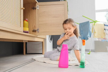 Cute little girl with bottles of detergent in laundry room. Child at risk