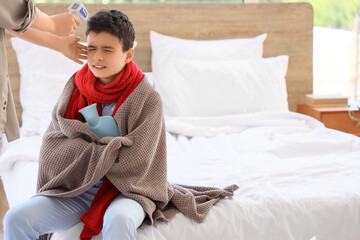 Mother with infrared thermometer measuring her ill son's temperature in bedroom